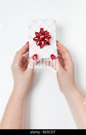 Close up of womans mains et belle boîte cadeau rouge blanc sur fond blanc. Mise à plat, vue du dessus Banque D'Images