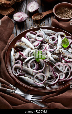 Anchois salé mariné à l'oignon rouge sur une plaque de faïence avec des olives, des graines de coriandre dans des bols et des tranches de pain de seigle sur un vieux bois rustique Banque D'Images