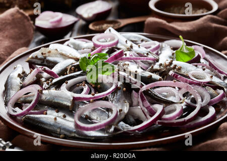 De chiffon sprats salés mariné à l'oignon rouge sur une plaque de faïence les graines de coriandre, brown tissu, fourchette et couteau sur une ancienne en bois rustique Banque D'Images