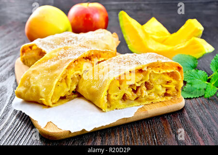 Citrouille Strudel aux pommes et aux raisins sur parchemin, menthe, fruits et légumes sur une planche en bois foncé Banque D'Images