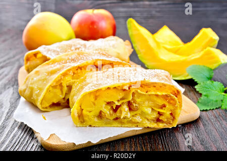 Citrouille Strudel aux pommes et aux raisins sur parchemin, menthe, fruits et légumes sur le fond de panneaux de bois Banque D'Images