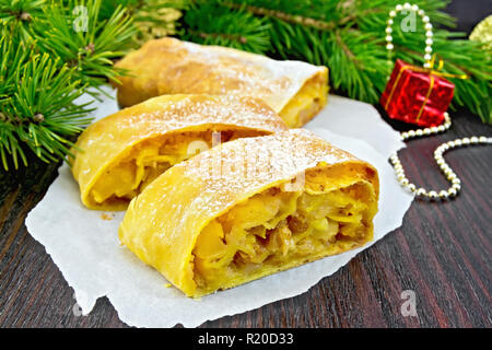 Citrouille Strudel aux pommes et aux raisins sur des parchemins, des branches de pins avec des jouets de Noël en arrière-plan d'une planche de bois Banque D'Images