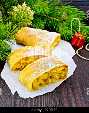 Citrouille Strudel aux pommes et aux raisins secs sur papier, des branches de pins avec des jouets de Noël en arrière-plan d'une planche de bois Banque D'Images