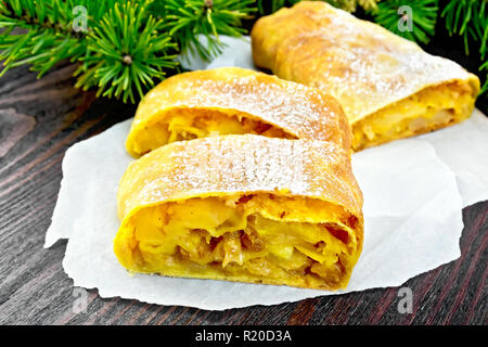 Citrouille Strudel aux pommes et aux raisins sur des parchemins, des branches de pins sur fond de planches en bois Banque D'Images