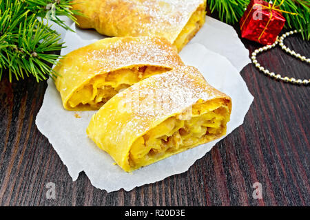 Citrouille Strudel aux pommes et aux raisins sur des parchemins, des branches de pins avec des jouets de Noël sur une planche en bois foncé Banque D'Images