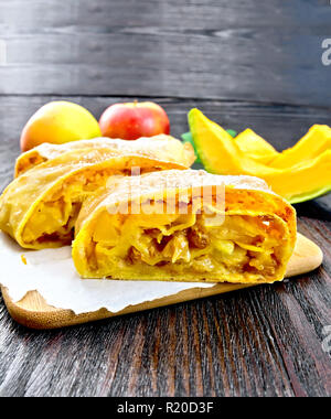 Citrouille Strudel aux pommes et aux raisins secs sur papier, des branches de pins avec des jouets de Noël en arrière-plan d'une planche de bois Banque D'Images