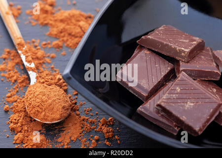 Casse le chocolat noir dans un bol noir et de poudre de cacao. Close up. Banque D'Images