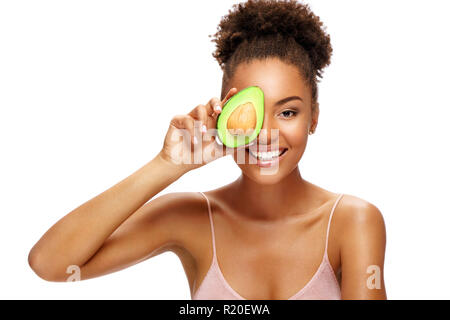 Jolie Jeune femme tenant une demi-avocat en face de son visage. Photo de smiling african woman isolated on white background. Beauté et Soins De La Peau d'hiver Banque D'Images