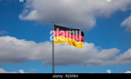 Brandir le drapeau allemand sur un mât contre ciel bleu avec des nuages, papier peint. Banque D'Images