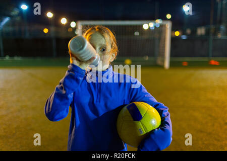 Girl soccer player en faisant une pause sur l'eau potable, domaine la nuit Banque D'Images