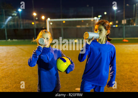 Les joueurs de soccer Girl Taking a break, l'eau potable sur la nuit sur le terrain Banque D'Images