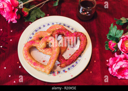 Churros en forme de coeur avec de la nourriture sur table rouge paillettes avec des fleurs pour la St Valentin Banque D'Images