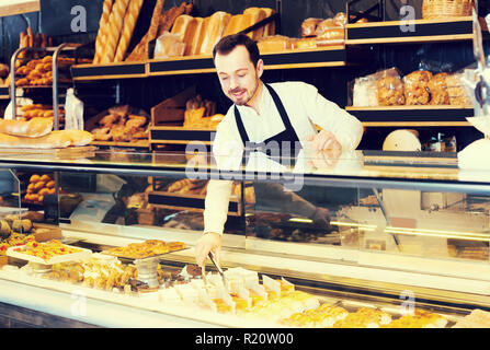 Young salesman montre les types de gâteaux dans une boulangerie Banque D'Images