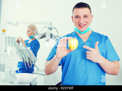 Smiling male dentiste Clinique Dentaire à poser avec des mains de pomme jaune Banque D'Images