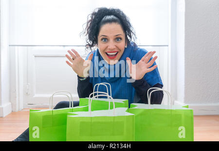 L'âge moyen femme aux yeux bleus, la peau blanche et les cheveux noirs faisant une drôle de surprise à l'expression à la caméra. De nombreux green shopping sacs remplis de cadeaux de Noël les soldes d'hiver Banque D'Images