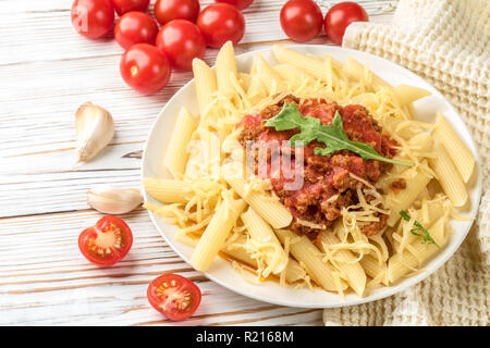 Les pâtes italiennes Penne bolognaise rigatone la viande hachée à la sauce tomate et de parmesan. Nature morte sur table en bois blanc, servi avec des tomates cerises, carafe d'huile d'olive et le verre de vin blanc Banque D'Images