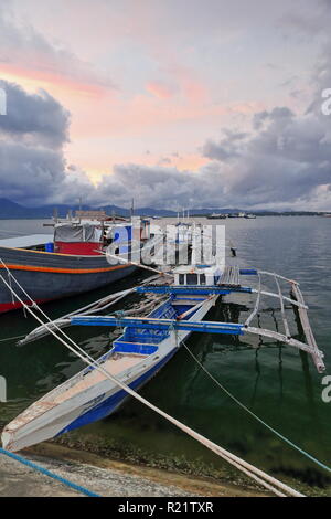 Pêche à balangay bangka ou double-bateaux pontés et outrigger bateau amarré à côté du port de commerce sur le quai le long de la ville Baywalk-orange Banque D'Images