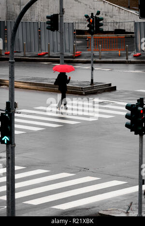 Femme marche sur le passage pour piétons dans la pluie avec parapluie rouge Banque D'Images