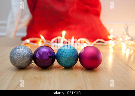Quatre boules scintillantes ou des ornements sur le plancher avec copie espace, lumières blanches et une rouge Santa Sack Banque D'Images