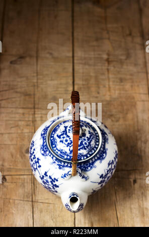 Théière en porcelaine blanc de Chine avec poignée en bambou et motif bleu sur fond de bois. Focus sélectif. Banque D'Images