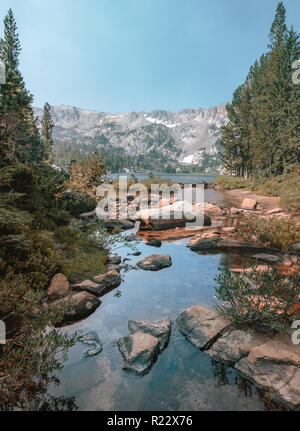 Reflet de l'eau ou un lac avec des pierres à l'avant-plan et d'arbres et d'une chaîne de montagnes et ciel bleu en arrière-plan. Banque D'Images