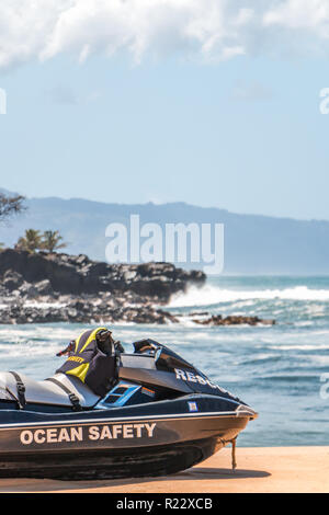 Life Guard jetski sauvetage est assis sur le sable à hawaii avec des vagues, des rochers, des maisons, et les nuages en arrière-plan. Composition verticale. Banque D'Images