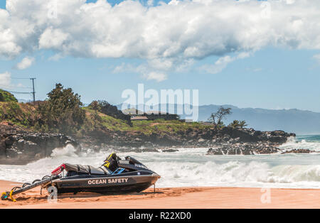 Life Guard jetski sauvetage est assis sur le sable à hawaii avec des vagues, des rochers, des maisons, et les nuages en arrière-plan. Composition horizontale Banque D'Images