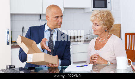 Représentant des ventes passant de carton avec des marchandises commandées à femme âgée dans la cuisine Banque D'Images