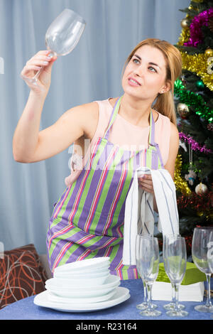 Jeune femme est serveing une table et l'essuyant des verres pour célébrer le Nouvel An à la maison. Banque D'Images