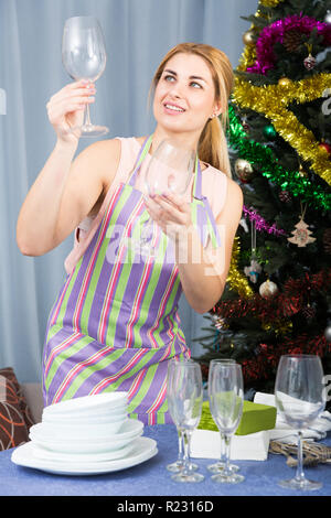 Jeune femme est serveing une table et l'essuyant des verres pour célébrer le Nouvel An à la maison. Banque D'Images