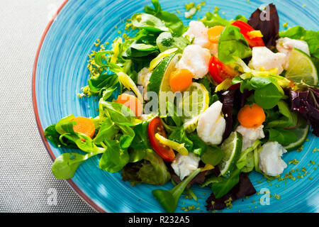 Hacher finement 200 grammes de merlu, faire mariner dans le jus de citron et poivre noir. Servi avec des feuilles de laitue, carottes fraîches et des rondelles de citron. Remplir d'huile et Banque D'Images