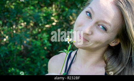 Portrait d'une jeune femme blonde normal caucasien visage avec des yeux bleu vert avec un sourire dans la nature fleurs Daisy Banque D'Images