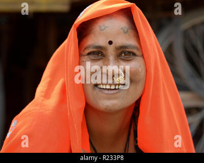 Middle-aged woman Rajasthani traditionnelle avec nez bijoux et tatouages tribaux sur le menton et le front porte un foulard orange (dupatta). Banque D'Images