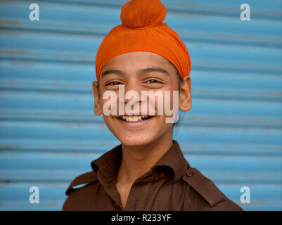 Sikh indien teen boy porte un sourire orange patka et pour l'appareil photo. Banque D'Images