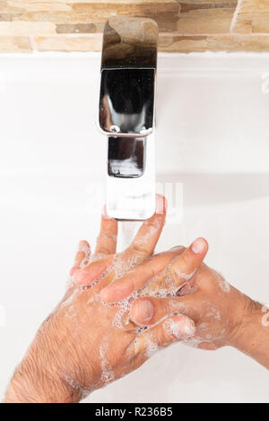 Personne mâle savonnage des mains au savon mousse sous un robinet d'eau Banque D'Images