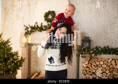 Happy mother and son petit fils jouent sur fond de l'arbre de Noël et guirlandes. Mère porte son fils sur ses épaules et ils Banque D'Images