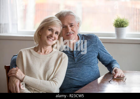 Portrait de famille de happy senior couple s'asseoir à la table d'accueil, de l'amour entre mari et femme embrasser qui pose pour photo, smiling elderly man tenir être Banque D'Images
