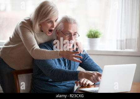 Mari et femme senior choqué en montrant l'écran du portable, de l'information incroyable voir couple âgé surprise inattendue avis sur ordinateur, elderl Banque D'Images