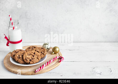 Cookies aux pépites de chocolat et de lait pour le Père Noël. Noël traditionnel, composé de biscuits, de bonbons de la canne à sucre et de la bouteille de lait avec un décor de Noël en bois blanc sur Banque D'Images