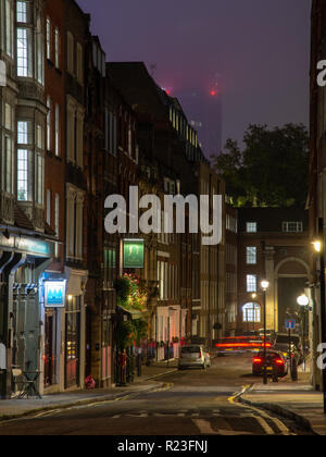 Londres, Angleterre, Royaume-Uni - Octobre 15, 2018 : Maisons et pubs de Londres le Temple d'un quartier sont éclairées la nuit, avec un gratte-ciel de la ville à demi caché dans la brume Banque D'Images