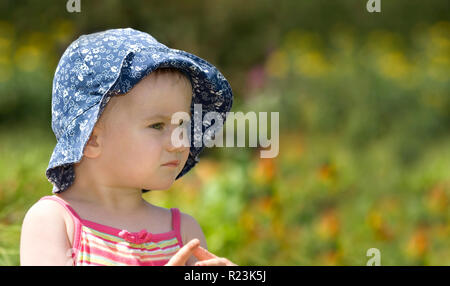 Cute little girl dans un cadre coloré et haut chapeau bleu sur champ vert, portrait panoramique Banque D'Images