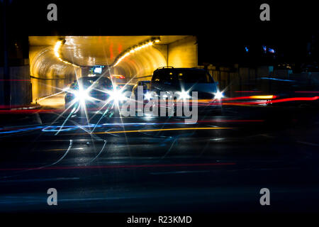 Le trafic de nuit dans les rues de la ville. Les voitures d'attente à la sortie du tunnel, à l'intersection d'attente alors que la conduite de véhicules déménagement passé laissant couleur light trails Banque D'Images