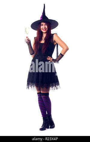 Photo de souriant sorcière avec un verre de vin avec du vin en robe noire et chapeau Banque D'Images