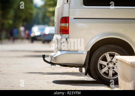 Close-up Vue de côté détail d'argent taille moyenne passager minibus de luxe van avec œillet de barre en stationnement sur la chaussée, rue de la ville ensoleillée d'été brouillée avec sil Banque D'Images