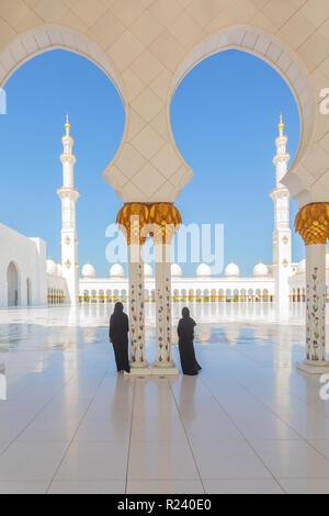 Deux (2) femmes portant des vêtements traditionnels Abaya noir admirant la beauté de la Grande Mosquée Sheikh Zayed à Abu Dhabi, Emirats Arabes Unis. Banque D'Images