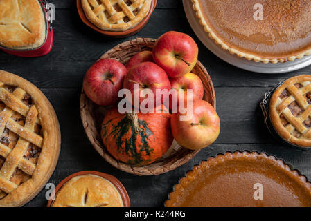 Voir ci-dessus de table de cuisine avec un panier en osier avec des pommes et des citrouilles au milieu, et diverses tartes traditionnelles, la citrouille de tartes et de tartes aux pommes. Banque D'Images