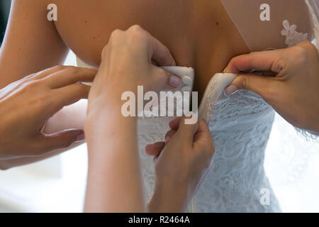Des mains amies aider la mariée à s'habiller de sa robe. Banque D'Images