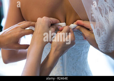 Des mains amies aider la mariée à s'habiller de sa robe. Banque D'Images