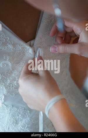 Des mains amies aider la mariée à s'habiller de sa robe. Banque D'Images