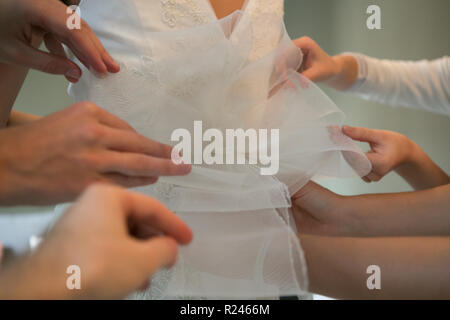 Des mains amies aider la mariée à s'habiller de sa robe. Banque D'Images